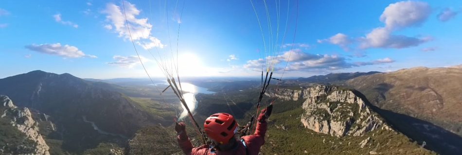Gleitschirmflieger schwebt über eine Berglandschaft mit blauem Himmel und Wolken.